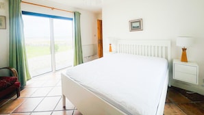 A hotel room with a bed, a nightstand, a lamp, a picture on the wall, and a view of the outdoors through a sliding door.