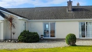 A modern two-story house with a grey tiled roof, large sliding glass doors, and a well-maintained lawn.