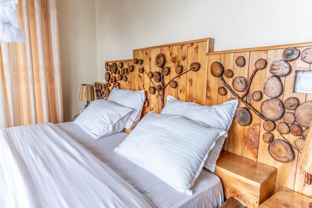 A double bed with white linens, a wooden headboard with a tree ring design, and a nightstand with a lamp.