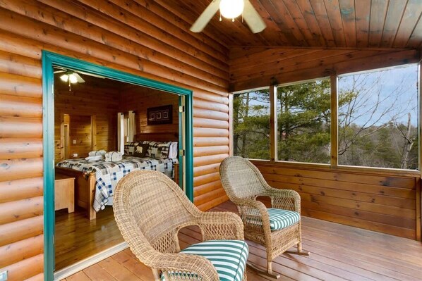 A log cabin with a bedroom featuring a bed, a chair, and a view through a window. - Mountain Retreat w/ Hot Tub & Fire Pit Oasis (Blue Ridge)