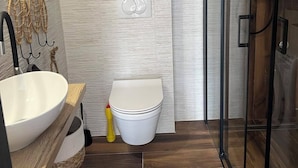 A compact bathroom with a white toilet, a sink with a wooden countertop, and a glass shower enclosure. - Apartman Suzzy 2 (Dramalj)