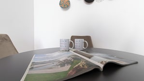 Une table avec deux tasses blanches ornées des logos d’Italianway, un magazine et un petit objet décoratif accroché au mur.