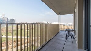 Un balcon avec vue sur un parc et des immeubles. On y trouve une table et des chaises.