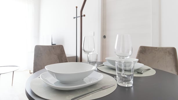 Une table à manger dressée avec des assiettes, des bols, des verres et des couverts blancs.