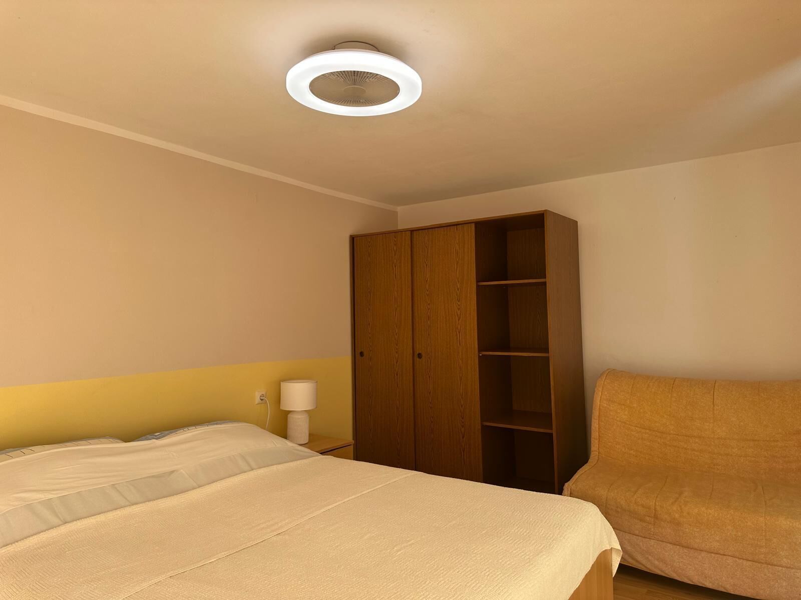 Ein Schlafzimmer mit einem Bett, einem Holzschrank, einer Nachttischlampe und einer Deckenleuchte.