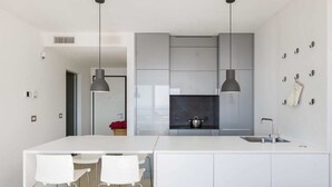 Une cuisine moderne dotée d’un îlot central, de luminaires suspendus et d’un plan de travail blanc.