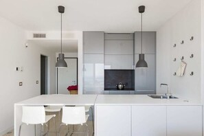 Une cuisine moderne dotée d’un îlot central, de luminaires suspendus et d’un plan de travail blanc.