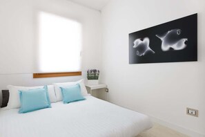 Une chambre à coucher avec un lit, des oreillers, une table de chevet, une œuvre d’art accrochée au mur et une fenêtre.