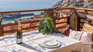 Une table dressée pour le dîner, avec une bouteille de champagne, des verres et des couverts, donnant sur une vue côtière et un paysage rocheux.