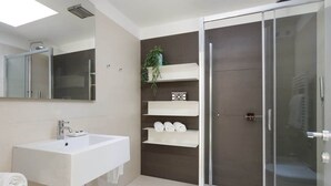 Une salle de bain moderne dotée d’un grand lavabo, d’une douche à parois de verre et d’étagères intégrées où sont rangées les serviettes.
