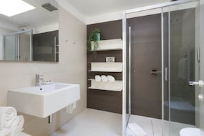 A modern bathroom with a large sink, a glass shower enclosure, and built-in shelves with towels.