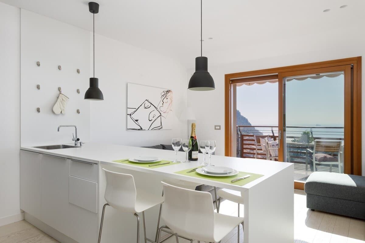 A modern kitchen with a central island, white cabinetry, pendant lighting, and a dining area with chairs.