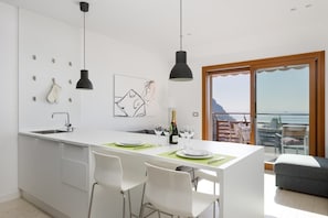 A modern kitchen with a central island, white cabinetry, pendant lighting, and a dining area with chairs.