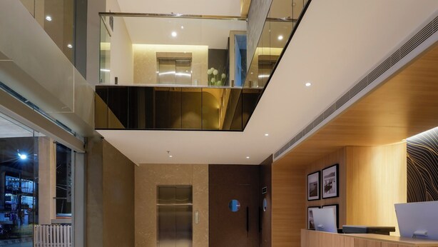 A modern hotel lobby with a marble reception desk, a glass elevator, and a mezzanine level with a wooden finish. - TGI Oberon  (Bengaluru)