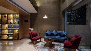 A modern lounge area with a blue sofa, red armchairs, a wooden bookshelf, and a round coffee table. - TGI Oberon  (Bengaluru)