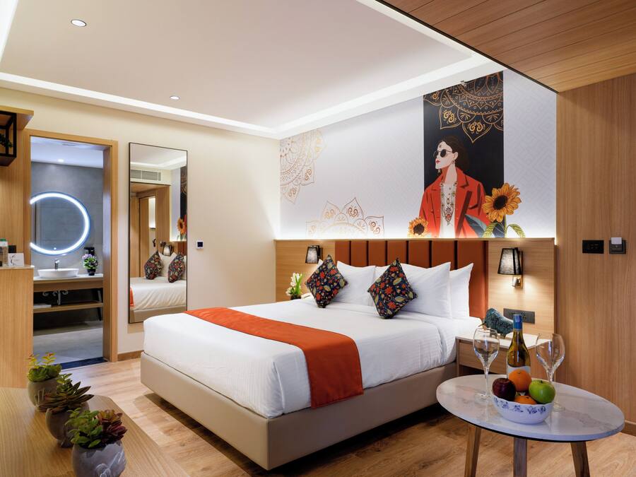 Una habitación de hotel moderna con una cama grande, una mesita de noche con copas de vino, un espejo y una pared decorada con un póster.