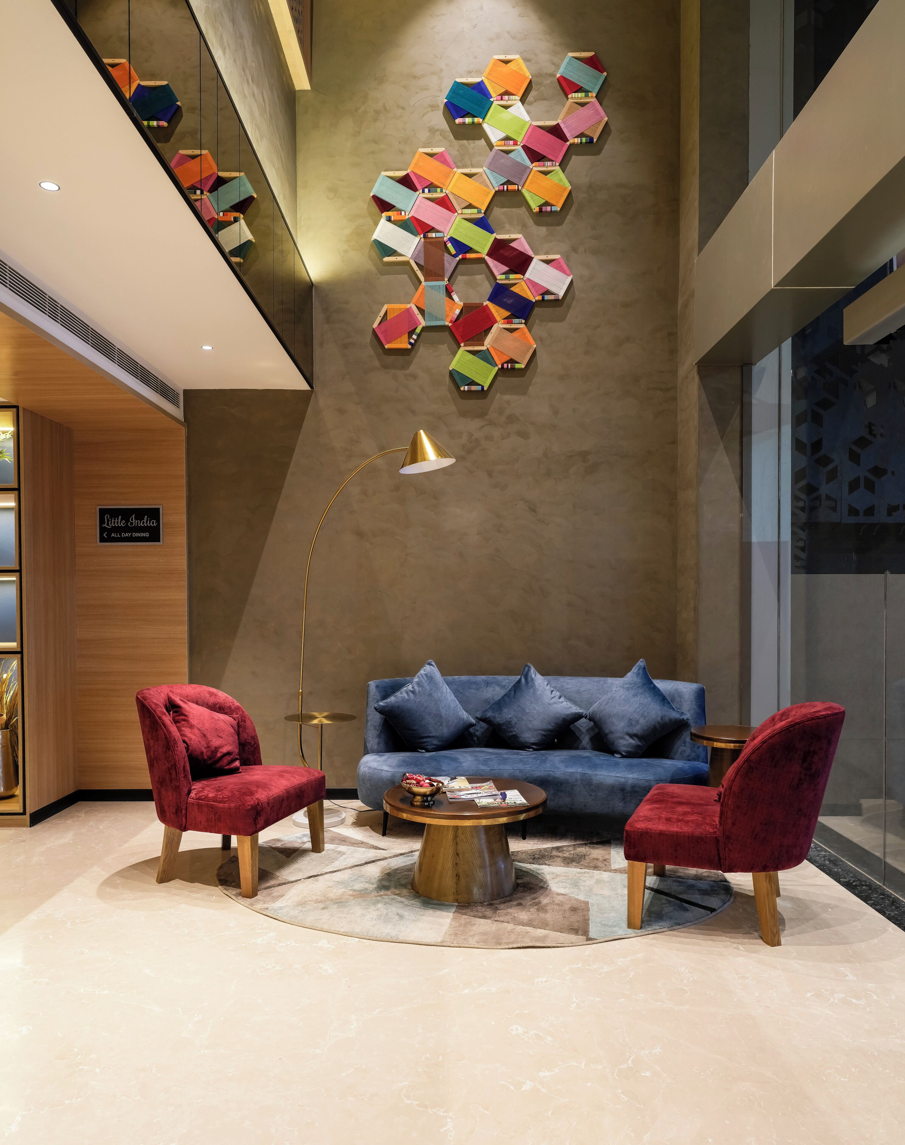 A modern lounge area with a blue sofa, red chairs, a wooden coffee table, and a geometric wall art installation.