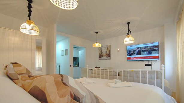 Une chambre d’hôtel avec un grand lit, deux lampes suspendues, un téléviseur fixé au mur et une vue sur le couloir.