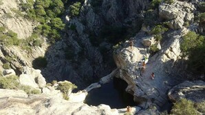A rocky landscape with a natural pool and people standing on the rocks.