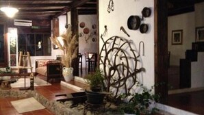 A rustic interior with a stone floor, a wooden ceiling, and a wall decorated with various kitchen utensils and plants.