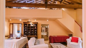 A cozy room with a high ceiling, a dining area with a table and chairs, a bookshelf, a bed with a red blanket, and a staircase. - Much loved by many: FIENILE, in the historic center, 7 km from the sea (Fermo)