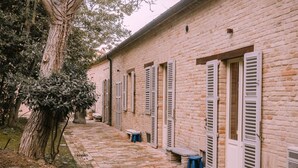 A brick building with white shutters, a paved walkway, and a tree. - Much loved by many: FIENILE, in the historic center, 7 km from the sea (Fermo)