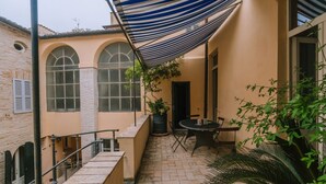 A courtyard with a table and chairs, a striped awning, and a potted plant. - Live in PALAZZO, historic center, 7 km from the sea (Fermo)