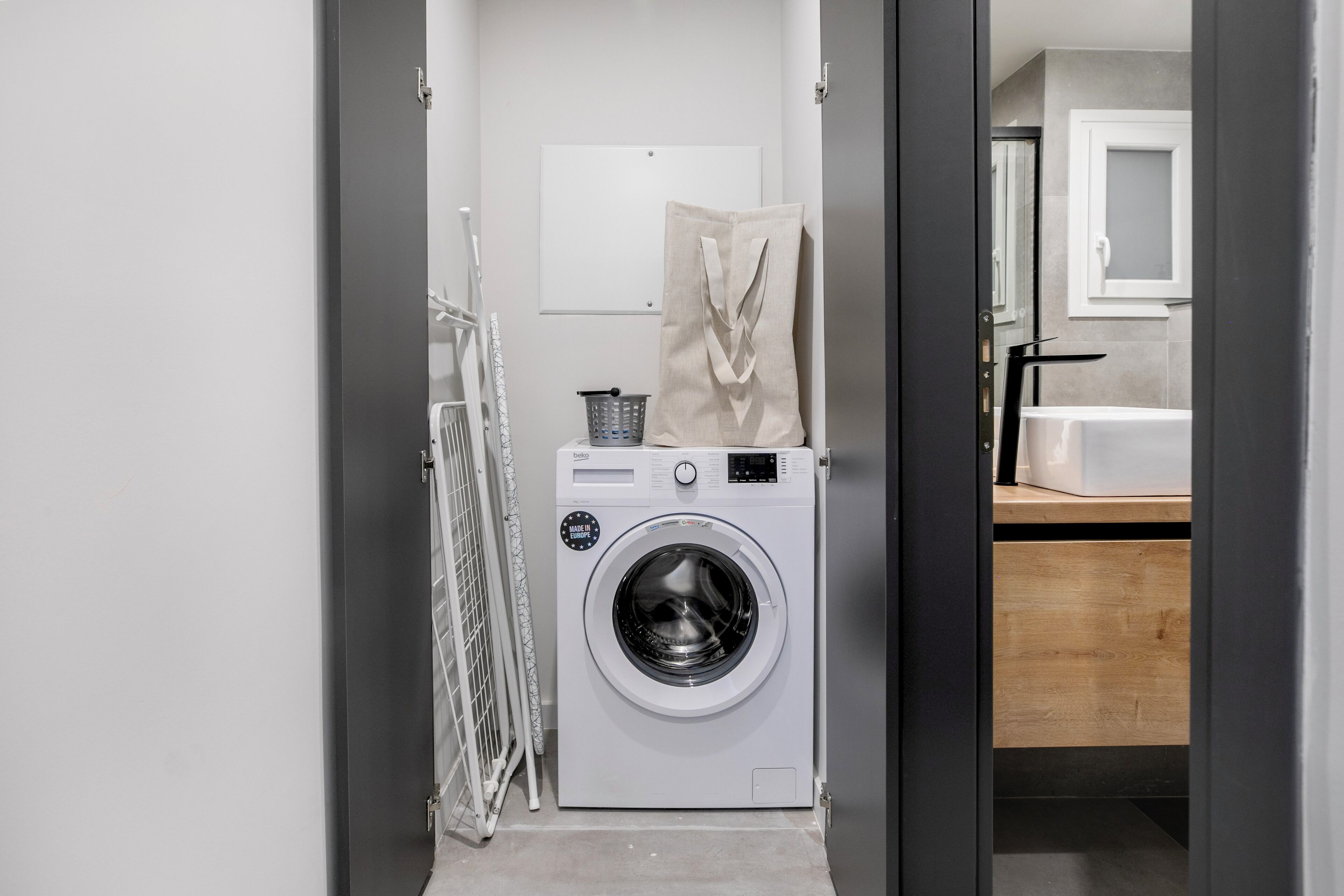 Une petite buanderie équipée d’un lave-linge à chargement frontal, d’un étendoir et d’un petit panier.