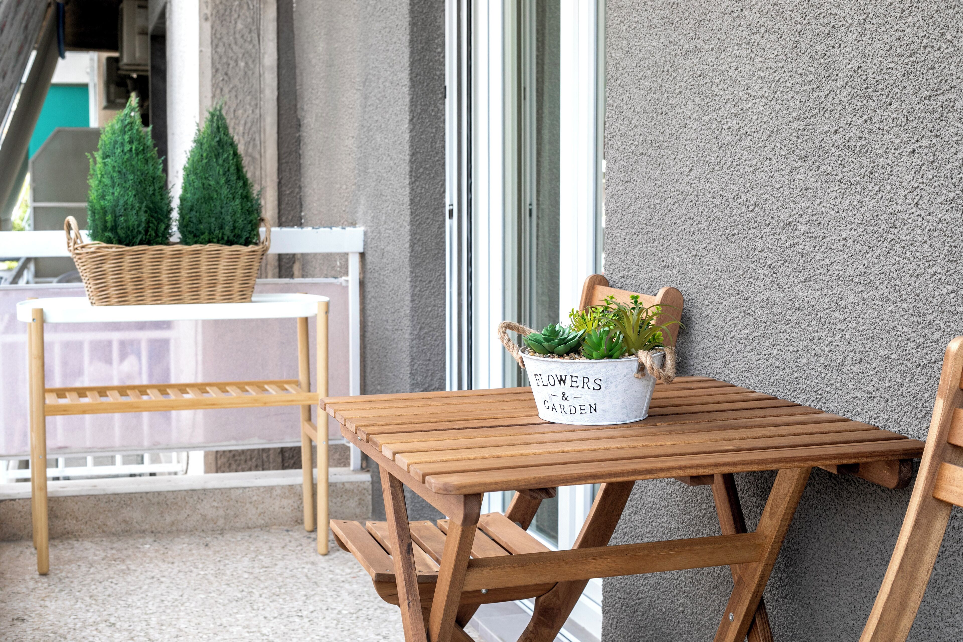Un conjunto de mesa y sillas de madera frente a una pared texturizada, con una cesta de mimbre y una planta en maceta sobre la mesa.
