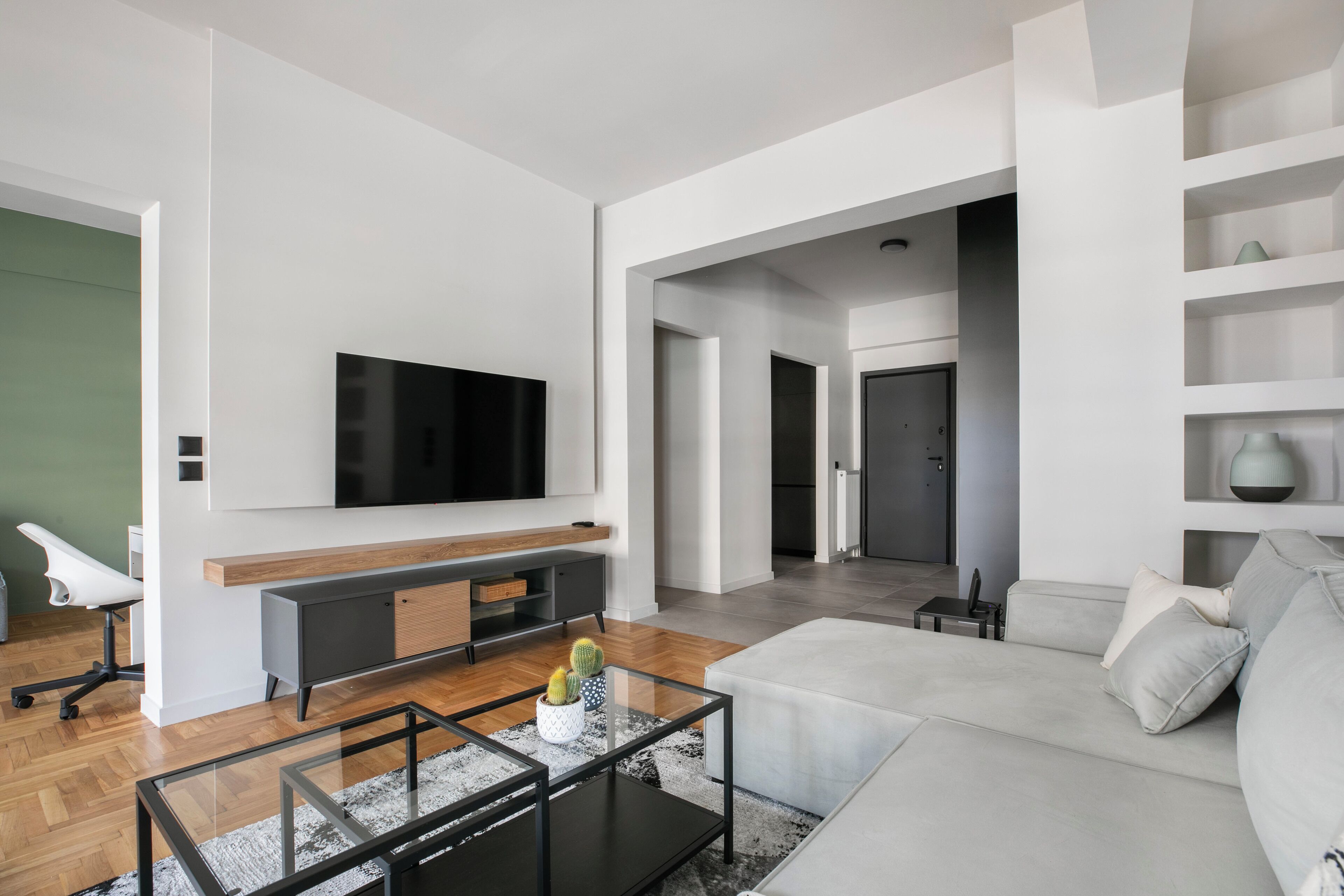 Een moderne woonkamer met een grote flatscreen-tv, een grijze bank, een salontafel en een minimalistisch design.