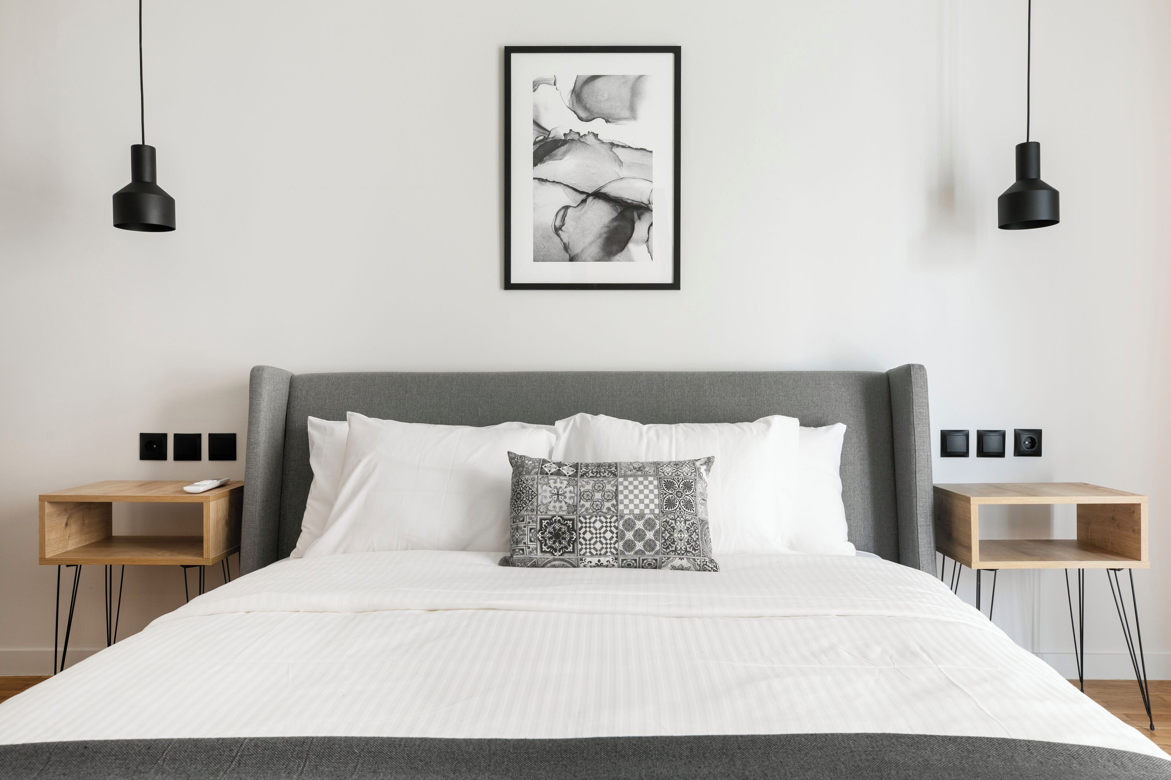 A neatly made bed with a patterned pillow, two bedside tables, and a framed artwork on the wall.