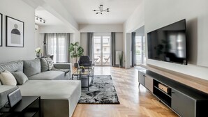 A spacious living room with a large flat-screen TV, a grey sofa, a coffee table, and a patterned rug. - Astoria -Luxury 2-BR Apartment in Athens (Athens)