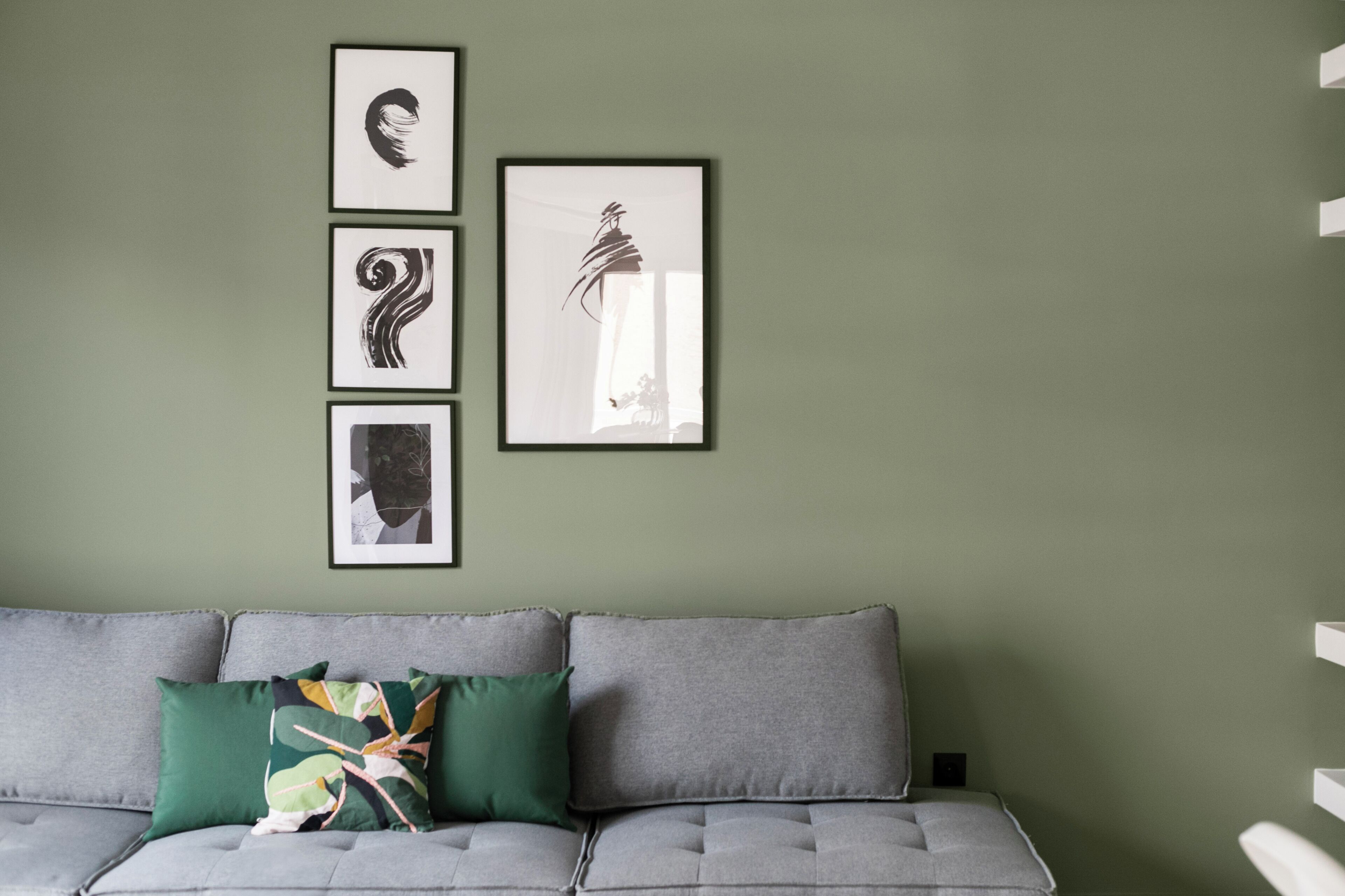 A grey sofa with a green pillow, a framed abstract artwork, and another framed artwork on a green wall.