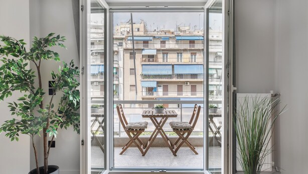 A balcony with a table and chairs, a potted plant, and a view of a residential building. - Astoria -Luxury 2-BR Apartment in Athens (Athens)