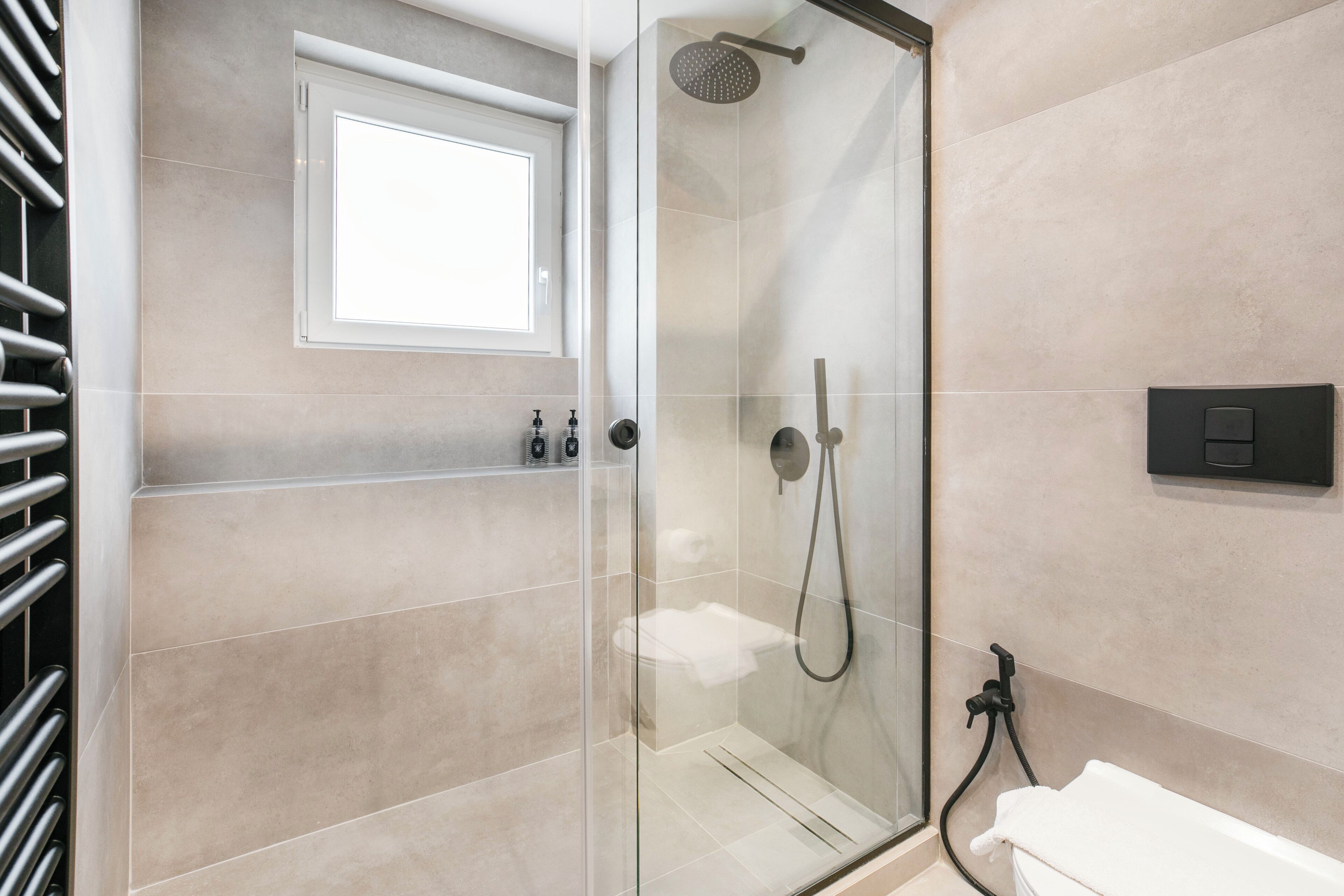 A modern bathroom with a glass-enclosed shower, a toilet, and a window.