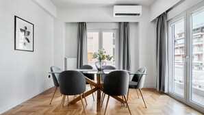 A modern dining area with a glass table, four chairs, and a vase of flowers. - Astoria -Luxury 2-BR Apartment in Athens (Athens)