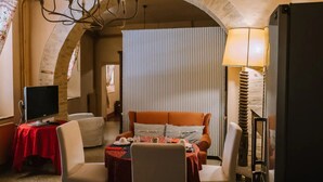 A cozy hotel room with a stone archway, a television, a dining area with a table and chairs, and a lamp. - In the city center, 7 km from the sea (Fermo)