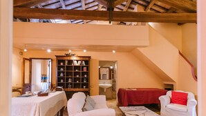 A cozy room with a high ceiling, a bookshelf, a dining table, a sofa, and a red-covered table. - House with a garden, downtown, 7 km from the beaches. (Fermo)