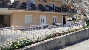 A two-story building with a balcony, a satellite dish, and a small garden area with flowers.