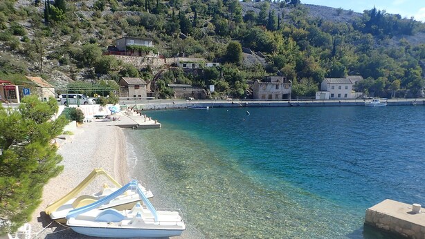 A clear beach with a boat docked on the shore, a parking area, and buildings in the background.