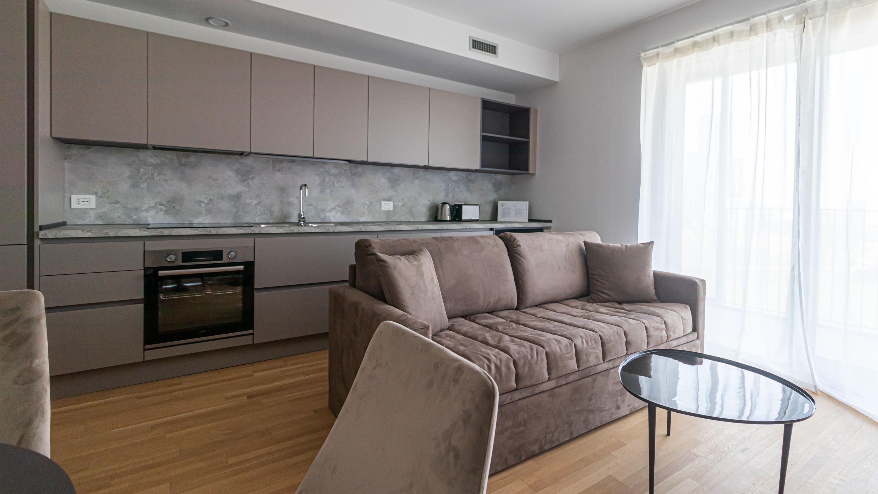 A modern kitchen with grey cabinets, a built-in oven, and a marble backsplash.