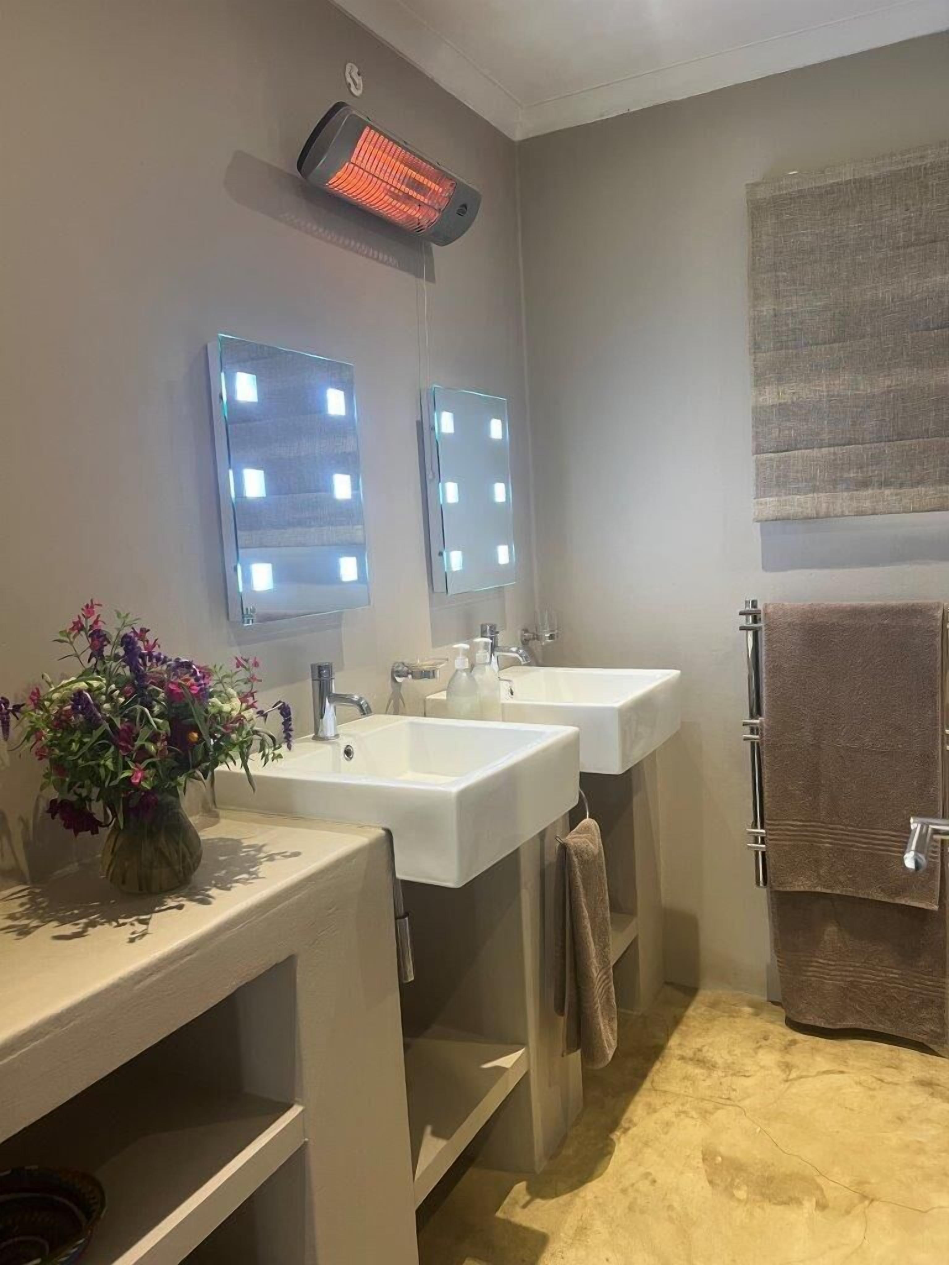 Un baño con dos lavamanos, un tendedero para toallas con calefacción y un espejo con iluminación.