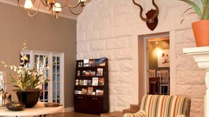 Eine Lobby mit Steinwand, einer Kristallleuchter, einem Bücherregal, einem gestreiften Sessel und einer Topfpflanze.