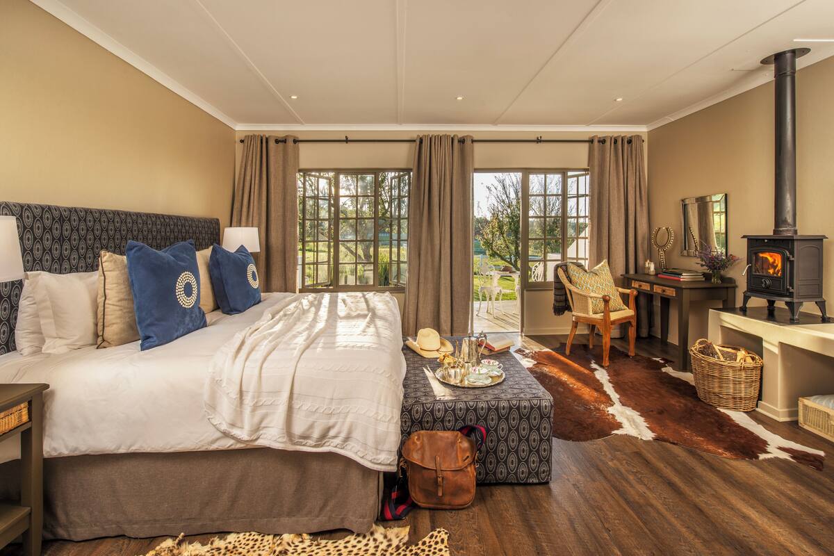 Un dormitorio espacioso con una cama grande, piso de madera, chimenea y vistas al exterior.