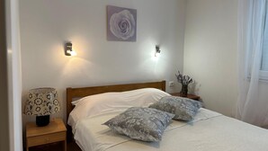 A bedroom with a bed, two wall-mounted lights, a nightstand with a lamp, and a wall-mounted flower painting. - Apartment Matkovic 3 (Jadranovo)