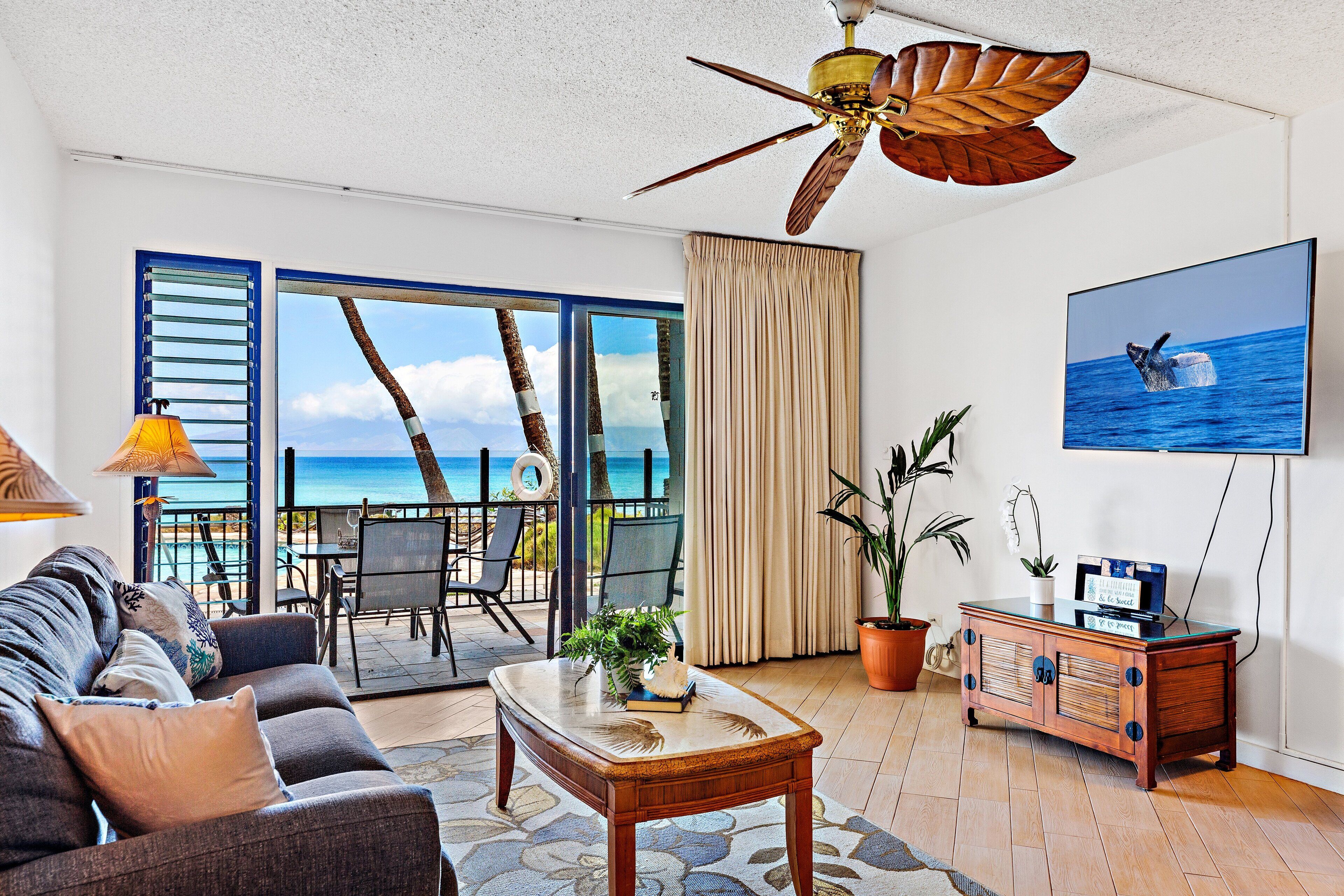 A living room with a sofa, coffee table, TV, and a view of the ocean.