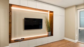 Un salon moderne avec un téléviseur à écran plat fixé sur un meuble blanc, des moulures en bois et une plante en pot.