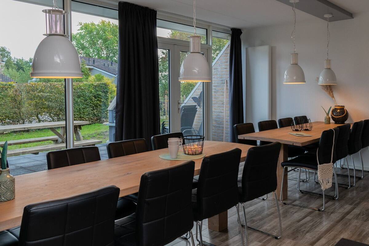 A modern dining area with a long wooden table, black chairs, and pendant lights.