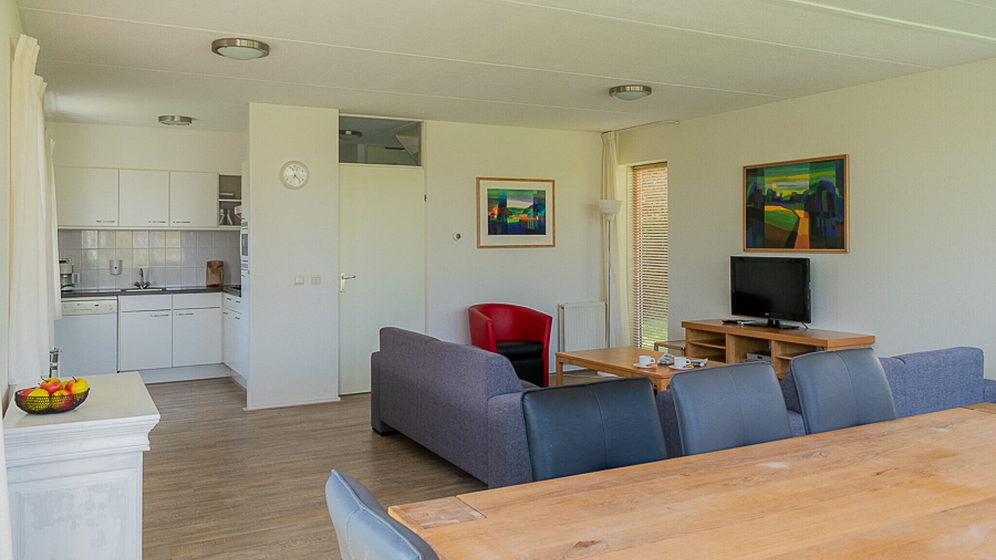 Een knus woongedeelte met een kitchenette, een eethoek met een houten tafel en een zithoek met banken.