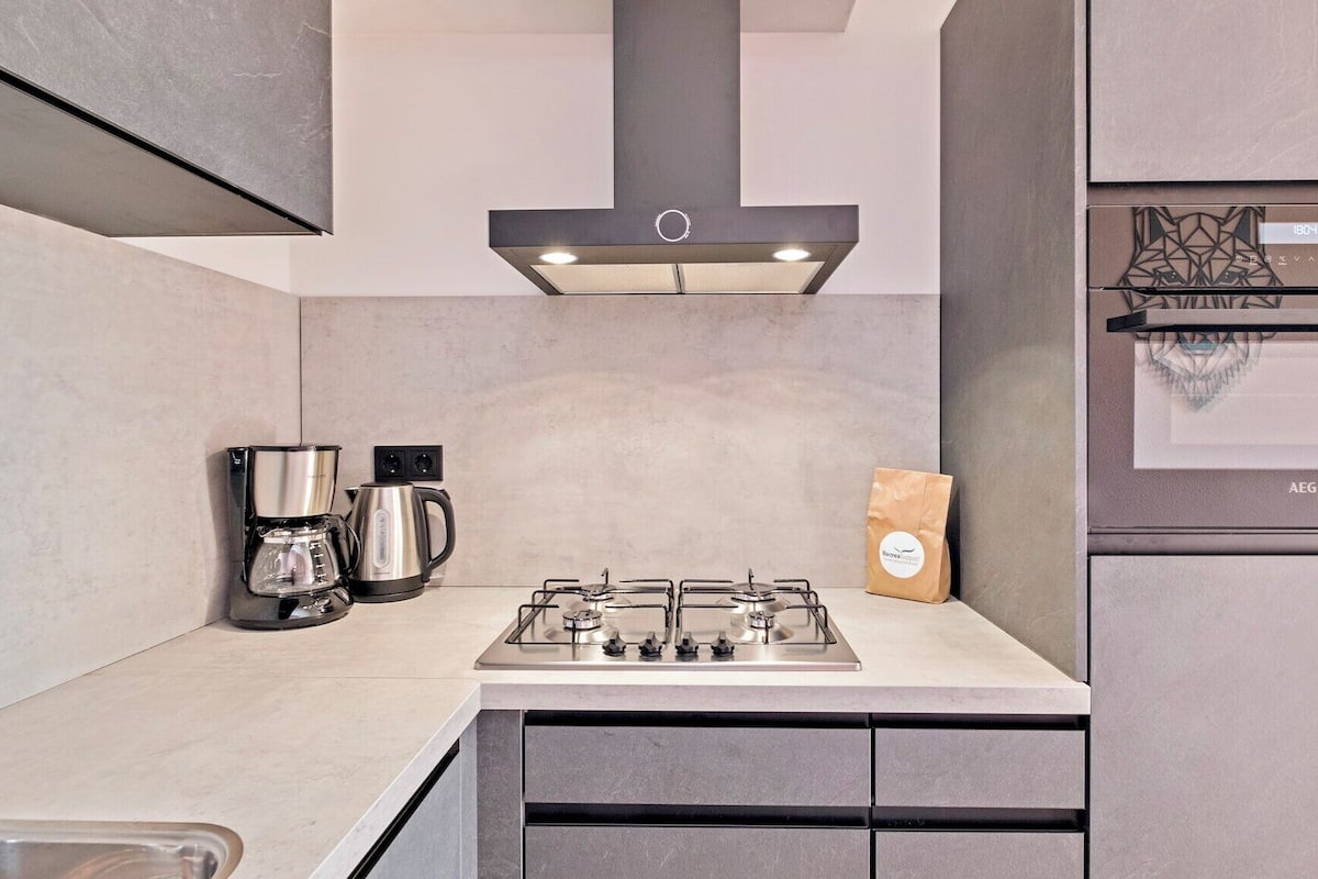 A modern kitchen with a gas stove, coffee maker, and a paper bag on the counter.